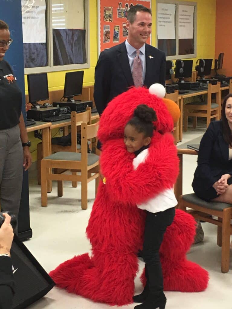 Elmo in the classroom hugging a student